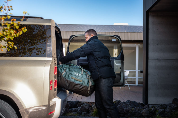 A man lifts an Osprey brand bag into the back of a car